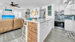 A modern kitchen with white cabinetry, a central island, and a dining area with a beige sofa.