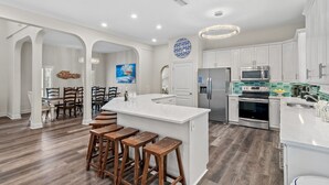 Una cocina amplia con armarios blancos, una isla central con taburetes y un comedor con sillas de madera.