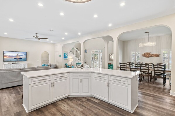 A spacious kitchen with white cabinetry, a large island, and a dining area with wooden chairs.