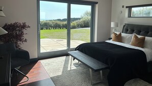 A modern bedroom with a large sliding glass door leading to an outdoor area, a bed with a grey headboard, and a bench by the door. - Spacious 6-bedroom house with WiFi, AC in enjoyable Dunmore East (Dunmore East)