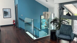A modern interior with a glass staircase, a blue accent wall, a framed artwork, a black chair, and a large window. - Spacious 6-bedroom house with WiFi, AC in enjoyable Dunmore East (Dunmore East)