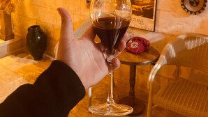 A hand holding a wine glass with a dark liquid, a vintage telephone, and various wall decorations in a warmly lit room.