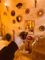Una mano sosteniendo una copa de vino con un líquido oscuro, un teléfono antiguo y varias decoraciones en una habitación con luz cálida.