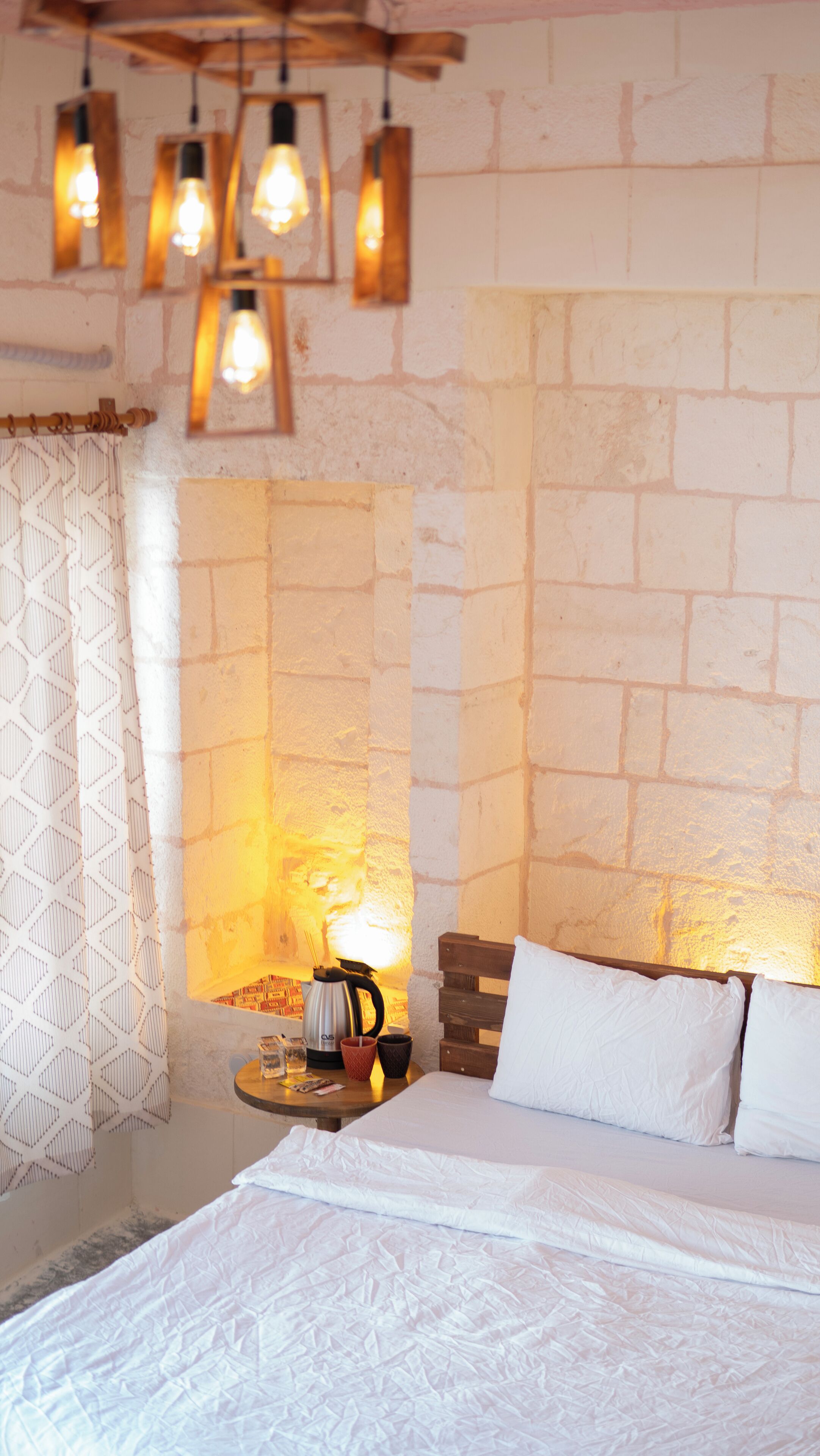 Una habitación acogedora con una cama, una mesita de noche con una tetera y una pared de ladrillo visto.