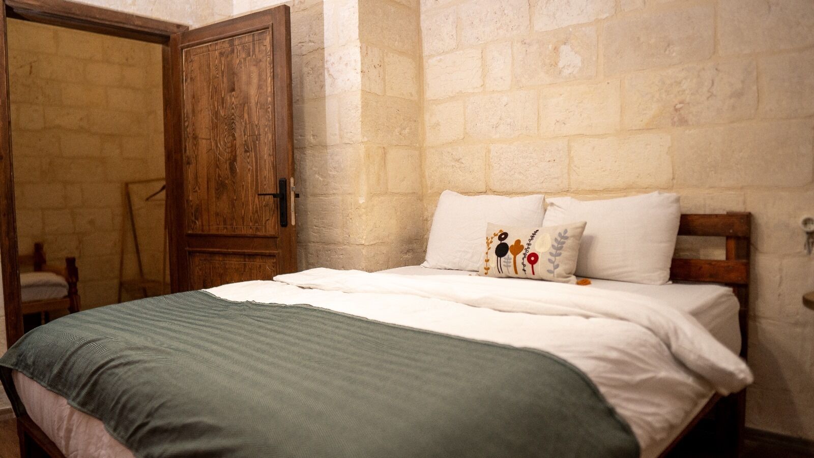 A bedroom with a wooden door, a bed with white bedding, and a green throw blanket.