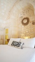 Un dormitorio con pared de piedra, puerta de madera y cama con ropa blanca y almohadas estampadas.