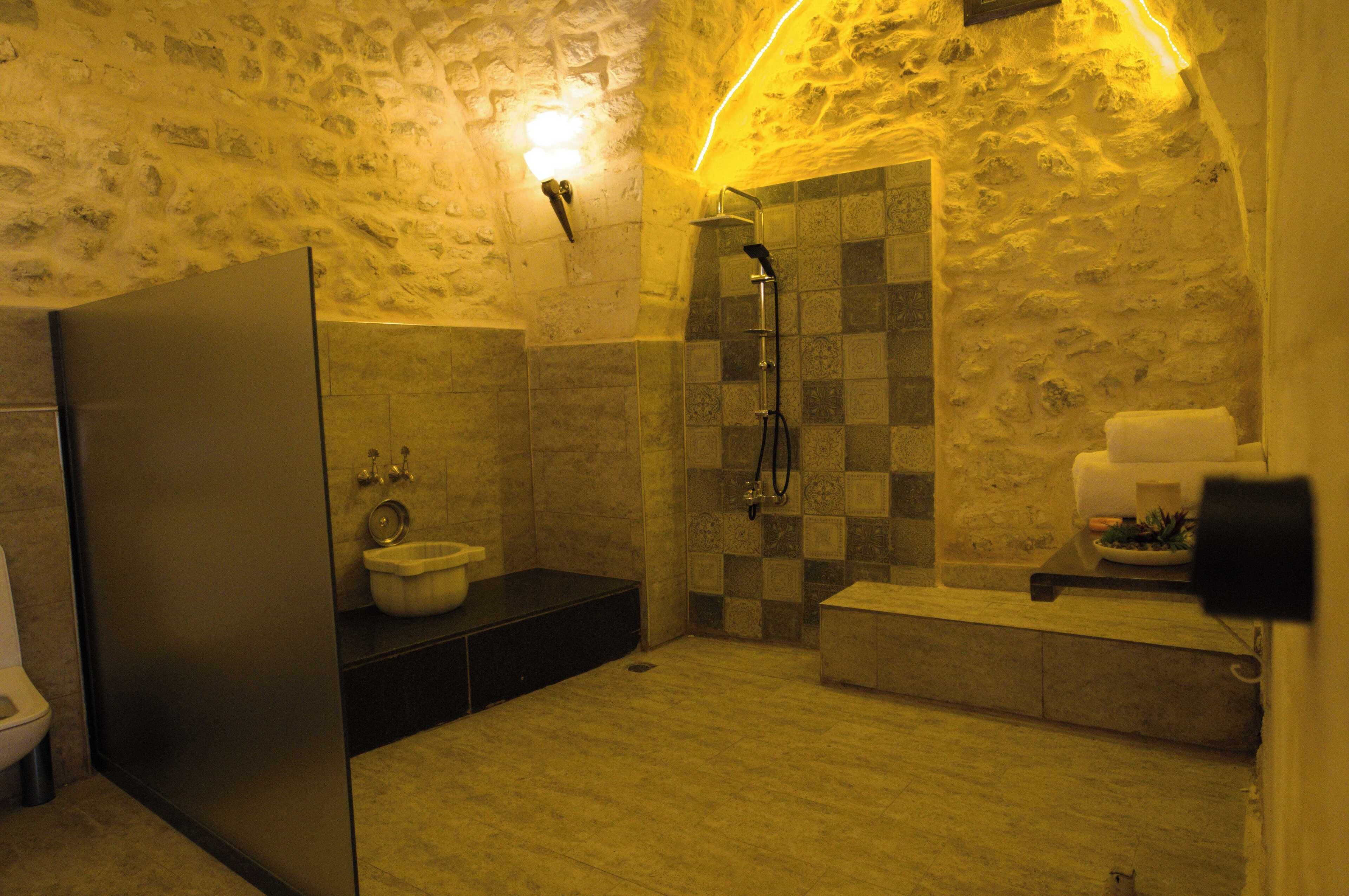 A bathroom with a stone wall, a shower, a toilet, and a sink.
