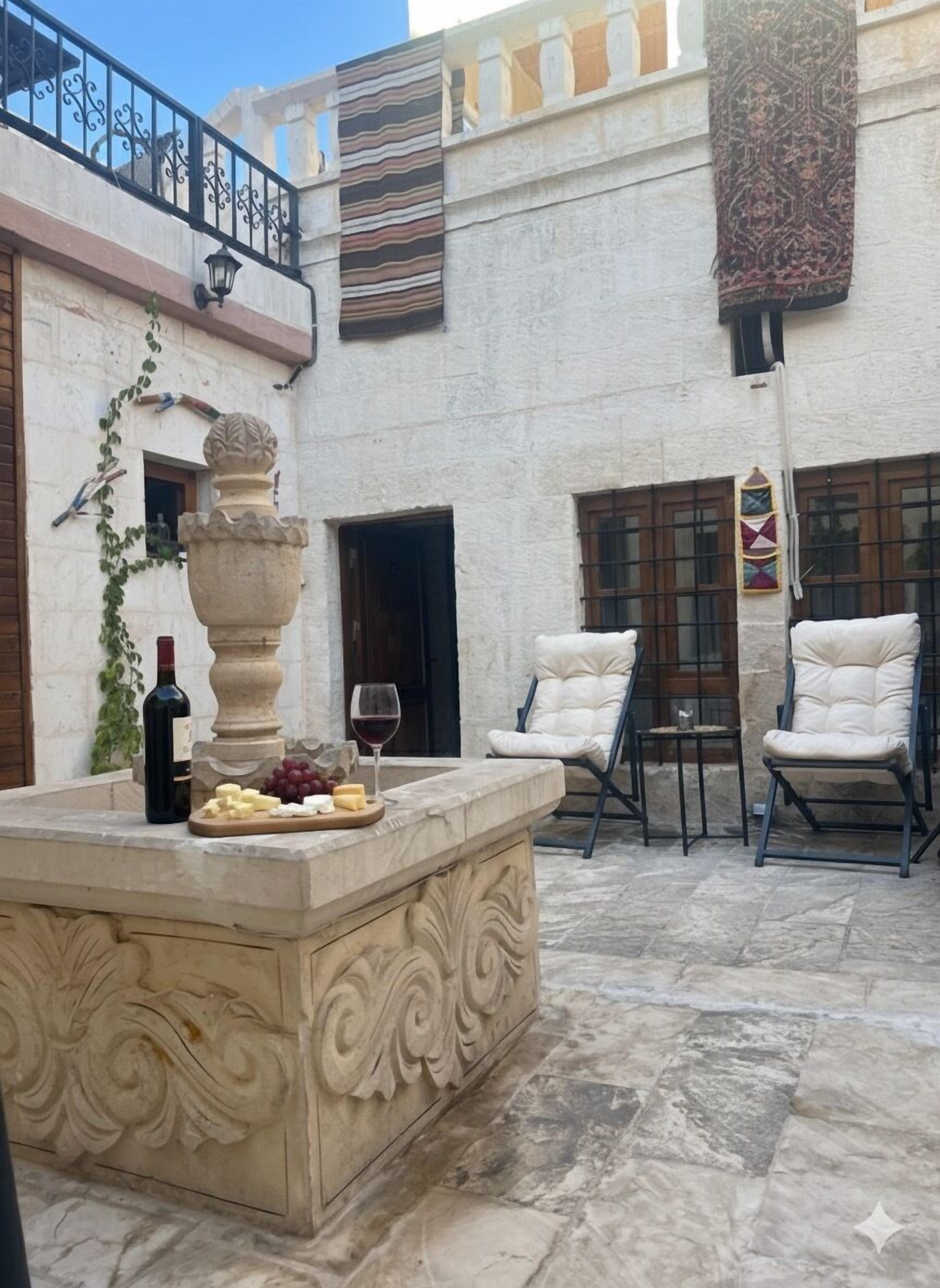 A courtyard with a marble fountain, seating area, and a wine bottle.