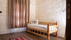 A single bed with a wooden frame and white bedding in a room with a brick wall and patterned curtains.