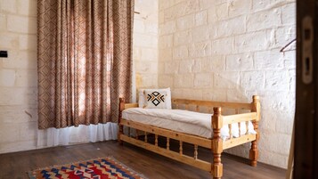 Una cama individual con estructura de madera y ropa de cama blanca en una habitación con pared de ladrillo y cortinas estampadas.
