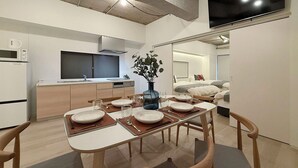 Una cocina moderna con microondas, estufa y lavaplatos. Hay una mesa de comedor con platos, vasos y cubiertos. Un televisor de pantalla plana grande está montado en la pared sobre la cocina.