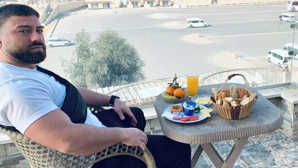Un homme est assis à une table, avec une pyramide en arrière-plan.