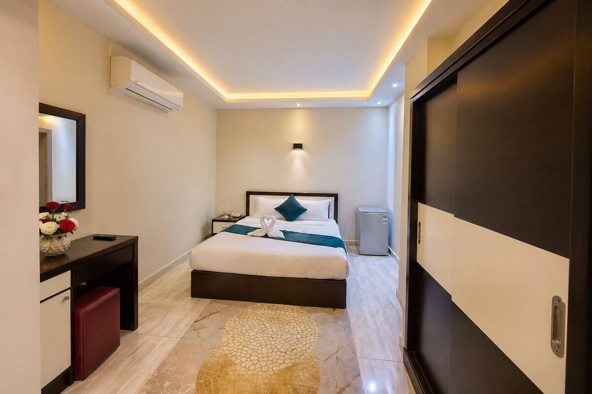 Una habitación de hotel moderna con cama, mesita de noche, equipo de aire acondicionado y un refrigerador pequeño.