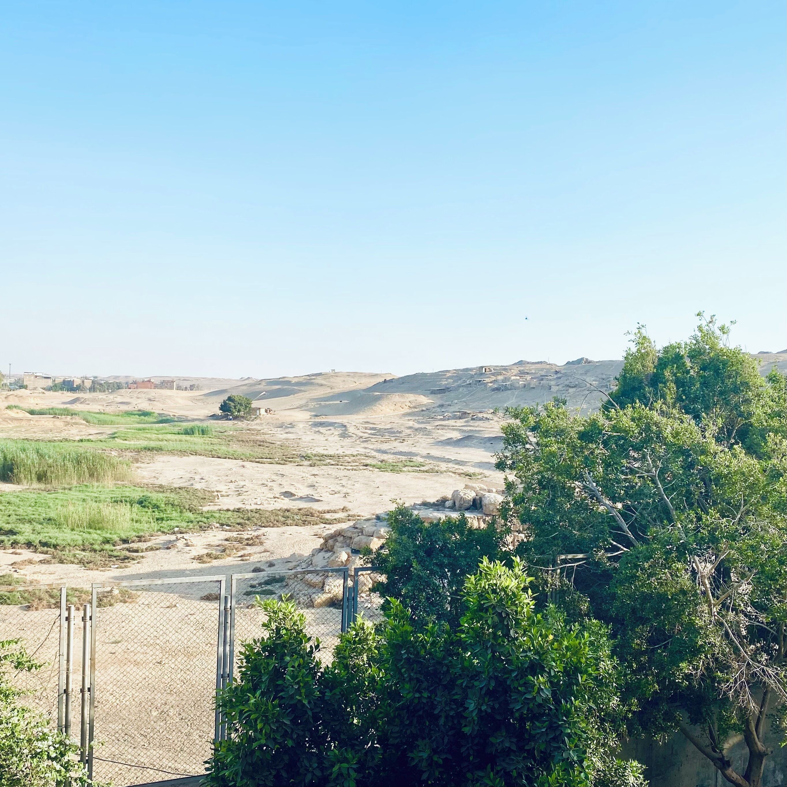 A rural landscape with a dirt road, sparse vegetation, and distant hills.