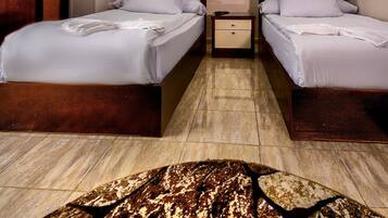 Habitación de hotel con dos camas, un armario de madera, una mesita de noche pequeña y una alfombra estampada.