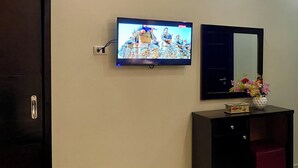 Une pièce avec un téléviseur fixé au mur, diffusant une émission, un miroir au-dessus d’une commode et une porte sur le côté gauche.