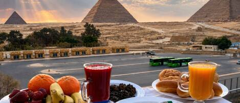 A table with food and drinks, a view of the pyramids, and a road with vehicles.