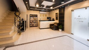 A hotel reception area with a reception desk, a clock, a poster, and a staircase. - Tut & Pyramids View (Giza)