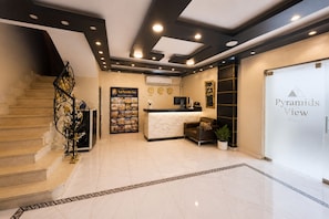 A hotel reception area with a reception desk, a clock, a poster, and a staircase. - Tut & Pyramids View (Giza)
