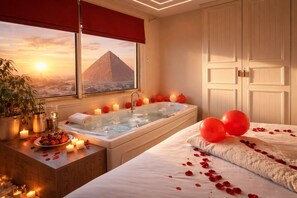 A room with a bathtub, a bed, a window with a view of a pyramid, and a potted plant. - Tut & Pyramids View (Giza)