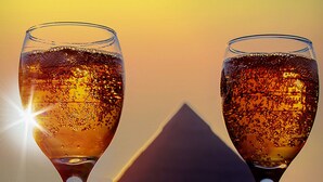 Deux verres à vin, avec un coucher de soleil et une montagne en arrière-plan.