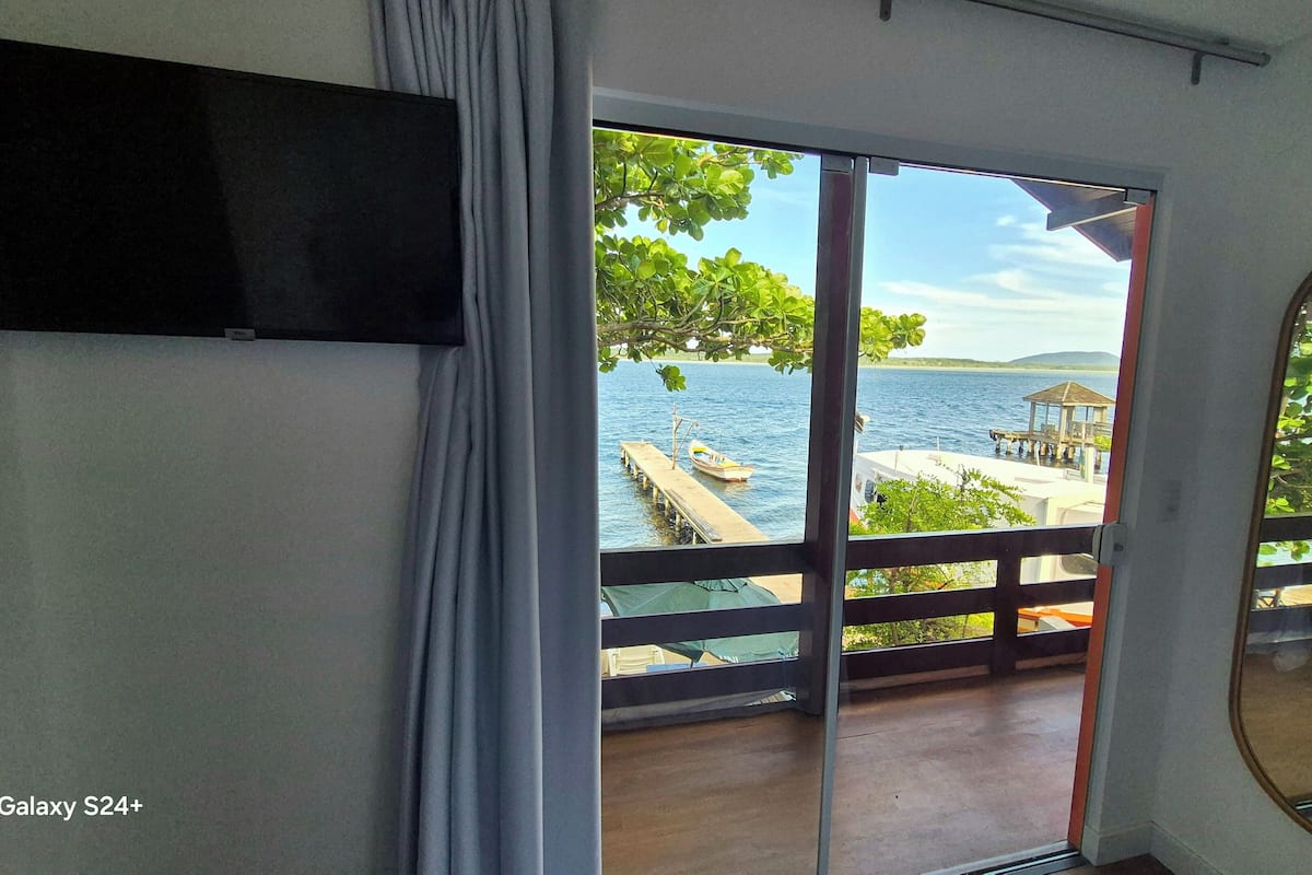 A room with a large sliding glass door leading to a balcony with a view of a lake and a dock.