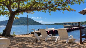 A beach with white chairs, a dock, and a boat. - Refugio Bela Ilha (Florianópolis)