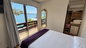 A bedroom with a bed, a wardrobe, a mirror, and a view of the sea through a sliding door. - Refugio Bela Ilha (Florianópolis)