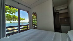 Habitación de hotel con cama, ventana grande con vistas a un cuerpo de agua y un pequeño balcón.