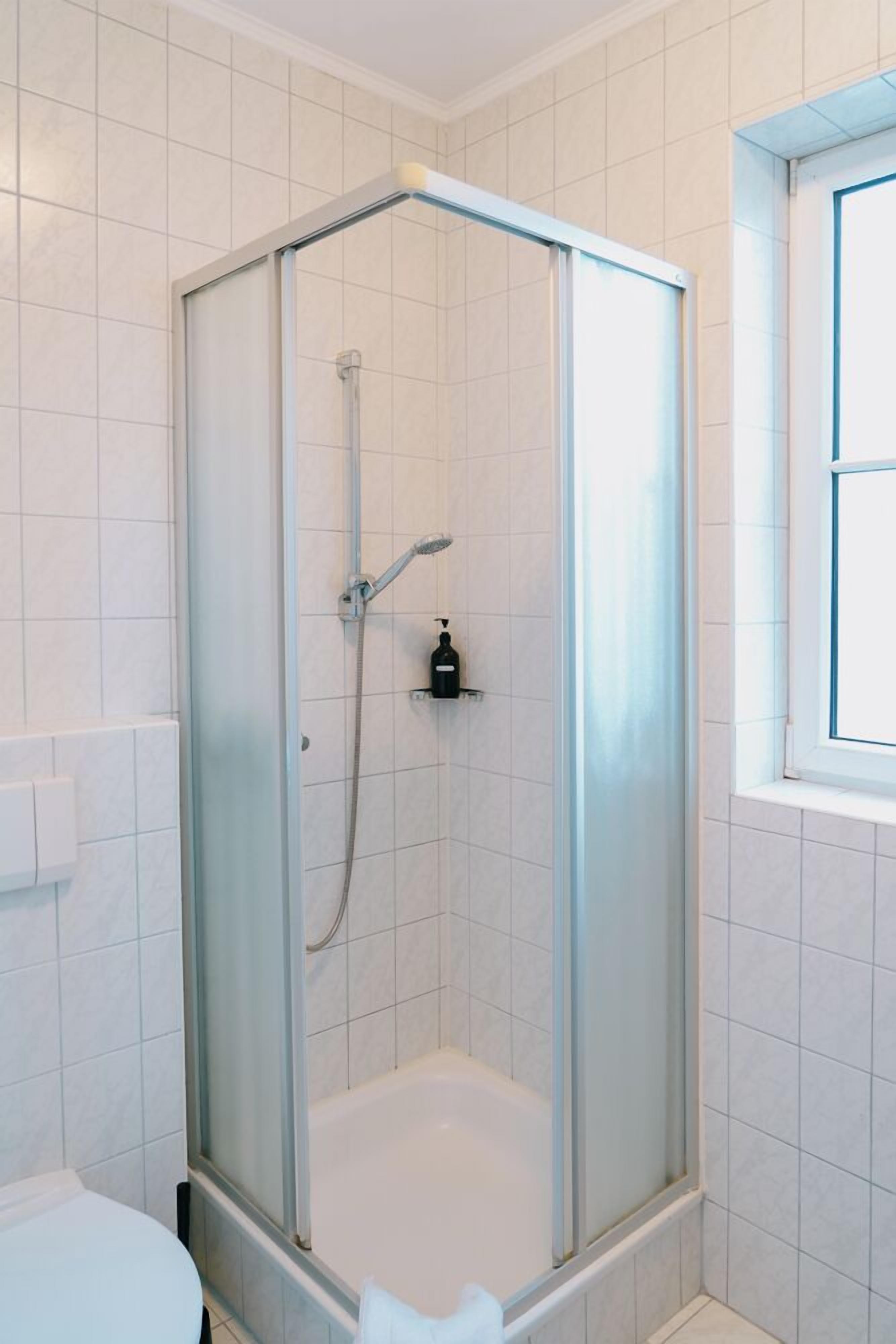 A modern bathroom with a glass-enclosed shower, white tiled walls, and a window.