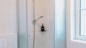 A modern bathroom with a glass-enclosed shower, white tiled walls, and a window.