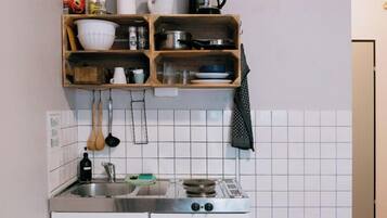 A compact kitchen with a white refrigerator, a small stove, and wooden shelves above the sink holding various kitchen items.