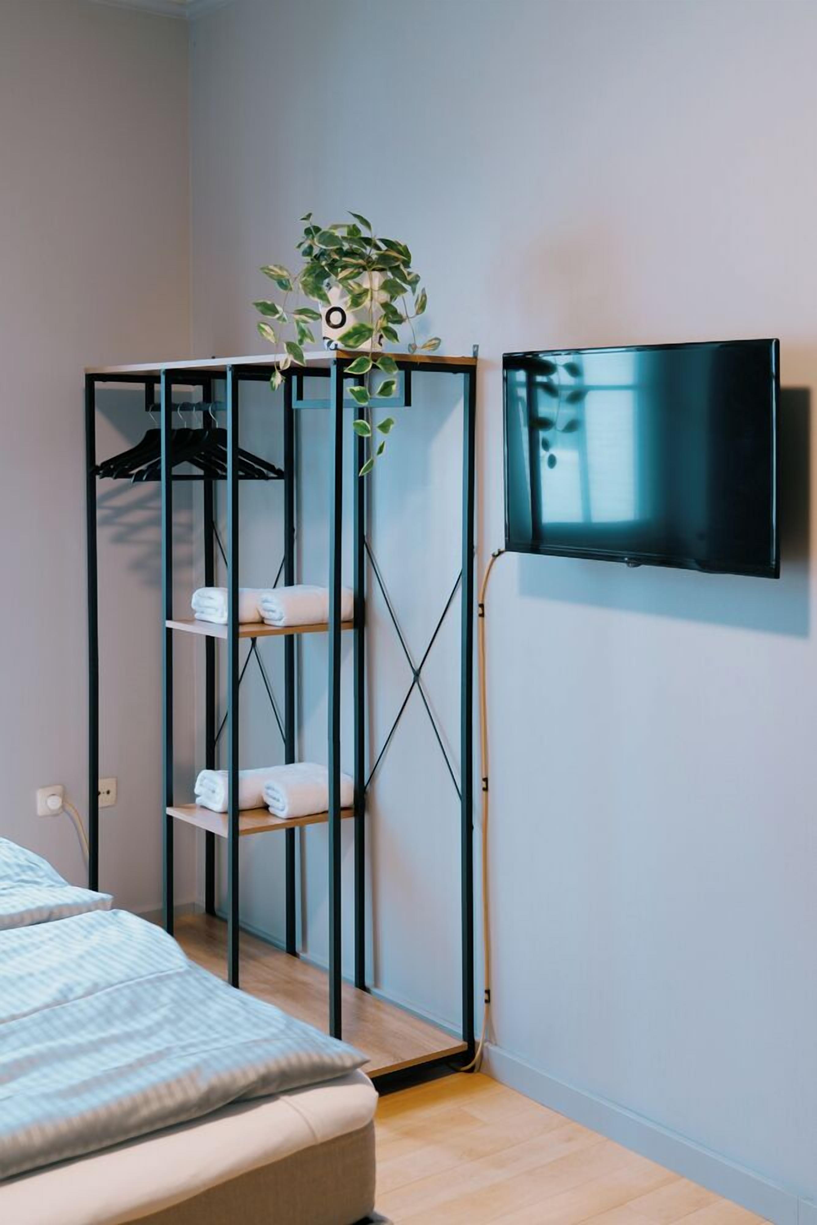 Une chambre à coucher avec un lit, une armoire avec des étagères, une plante et un téléviseur fixé au mur.