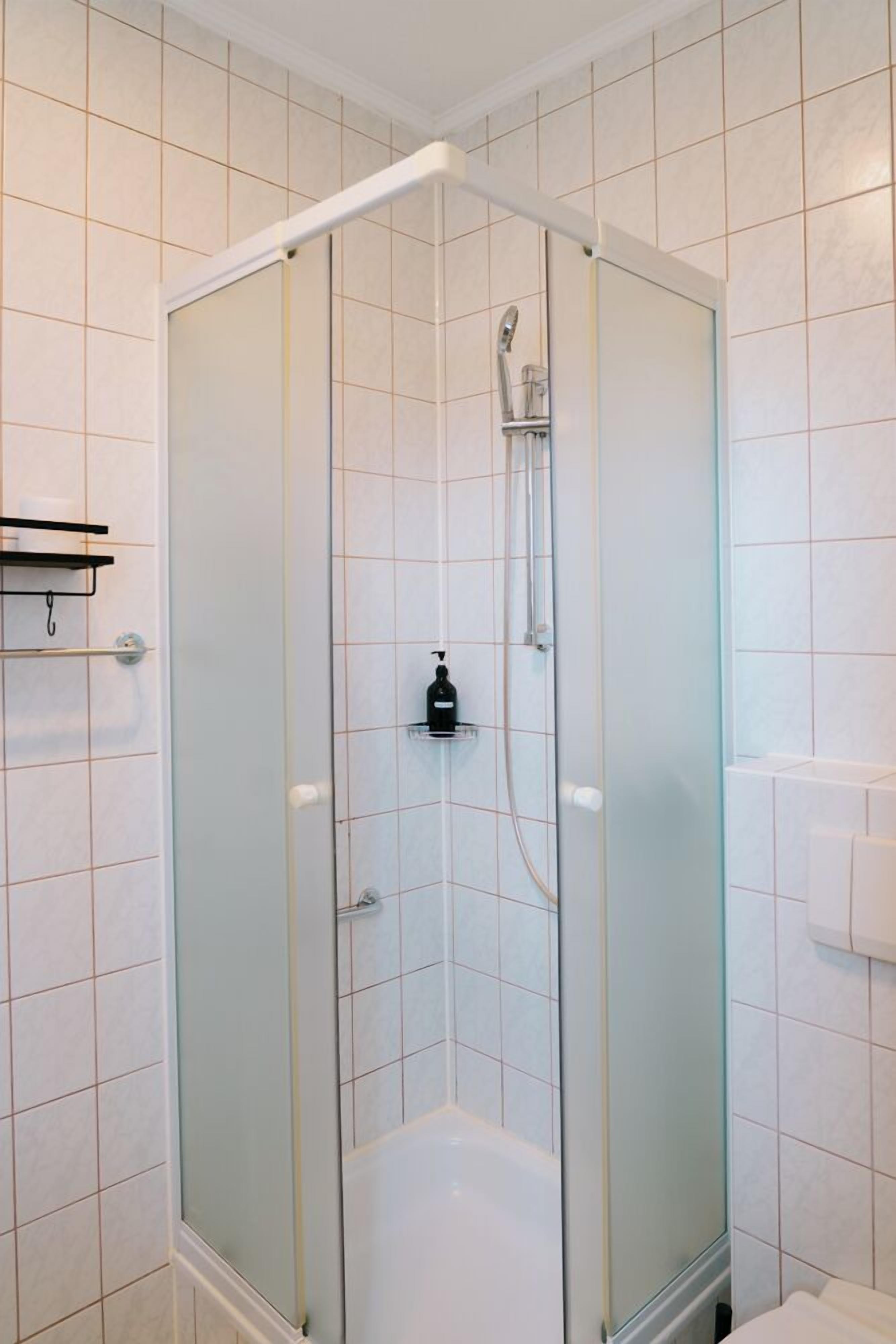Une cabine de douche fermée par des parois en verre, dotée d’un pommeau de douche à main et d’une bouteille de shampoing posée sur une étagère.
