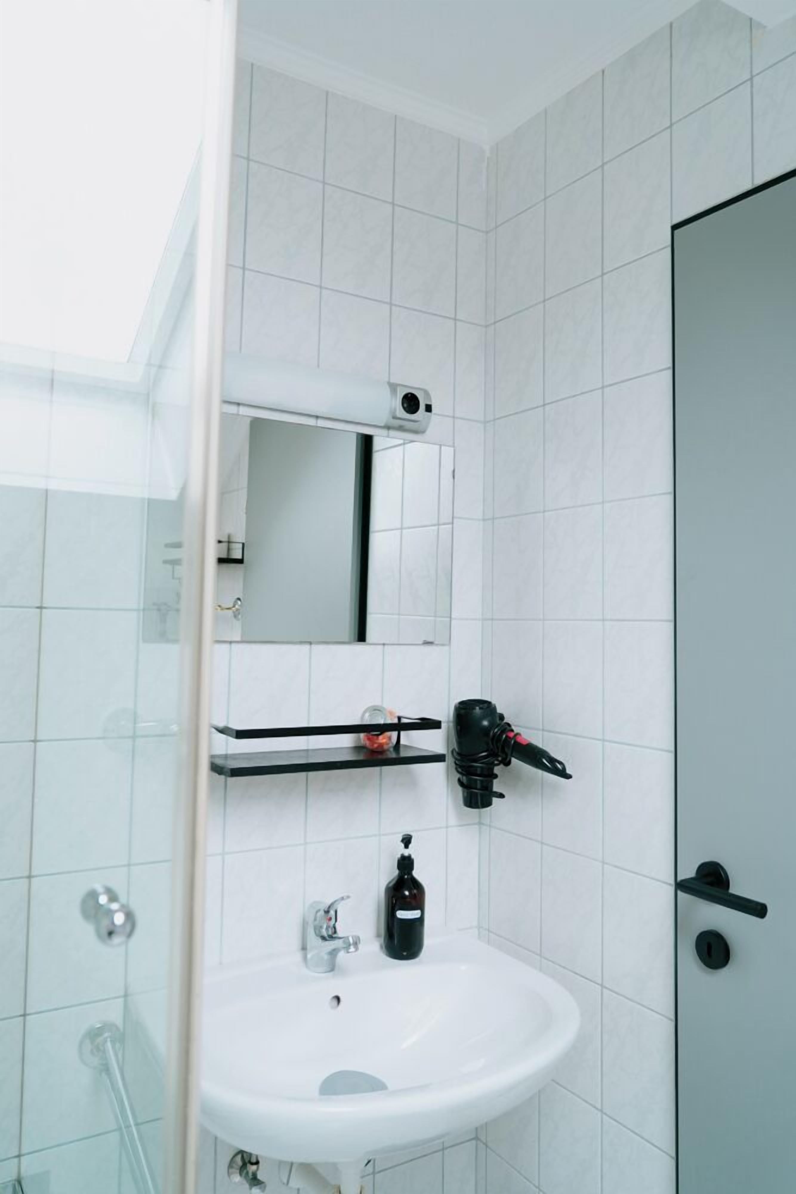 Un baño con lavamanos blanco, espejo, secador de pelo y cabina de ducha de vidrio.