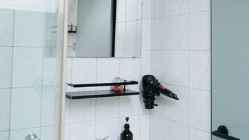 Un baño con lavamanos blanco, espejo, secador de pelo y cabina de ducha de vidrio.