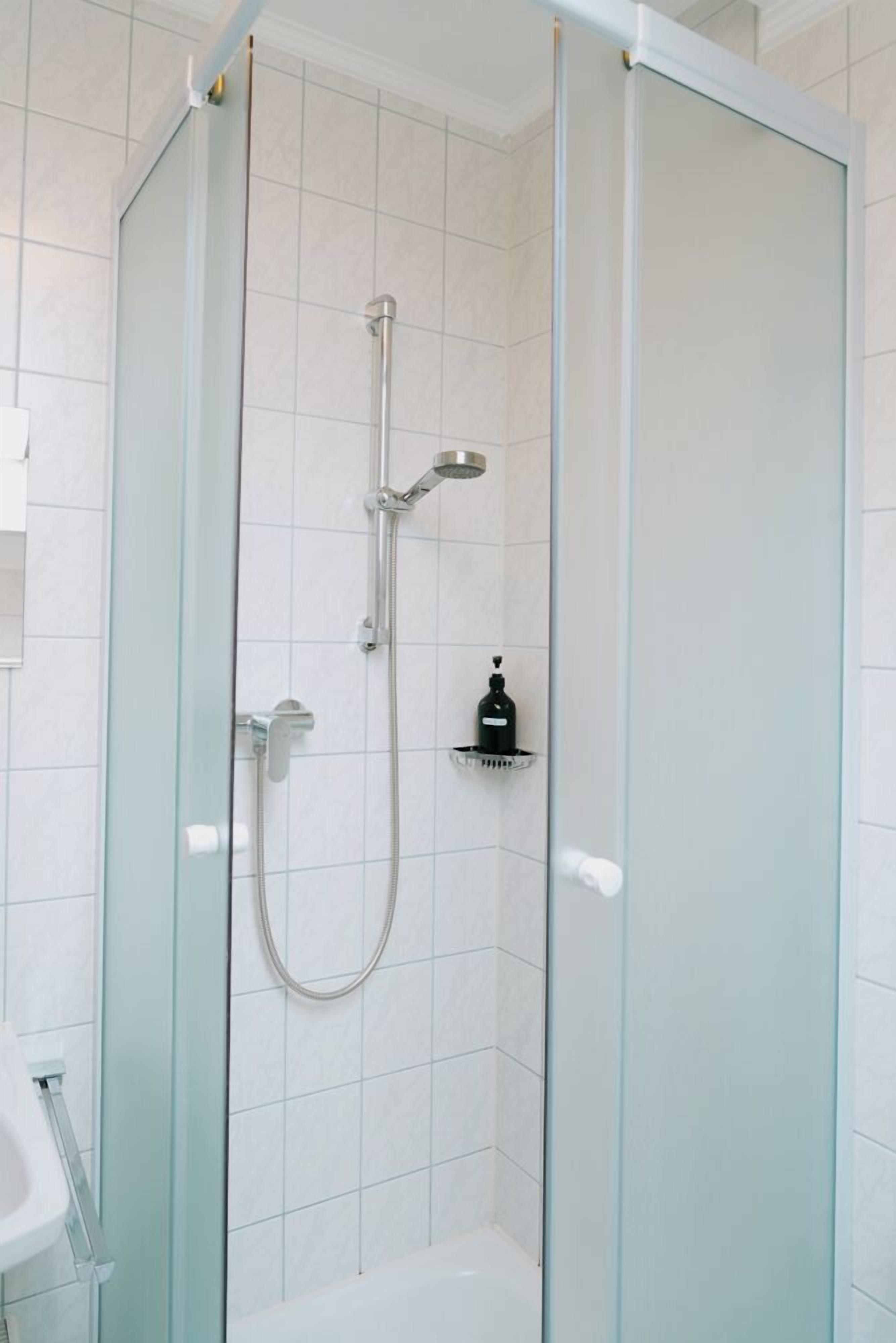 Un box de ducha con paredes de cristal, ducha de mano y grifo de mano.