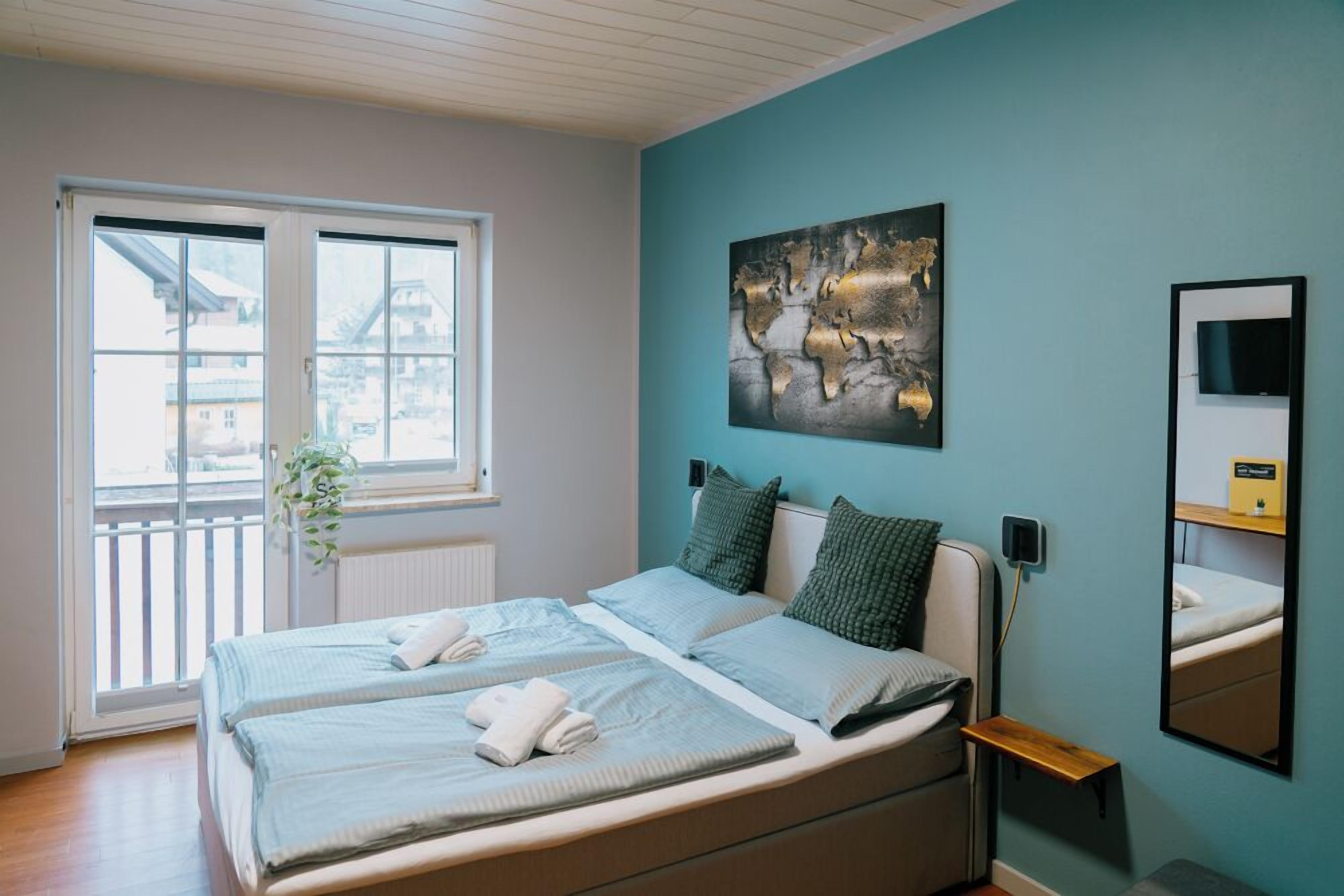 A bedroom with a bed, a window, a wall-mounted TV, and a mirror.