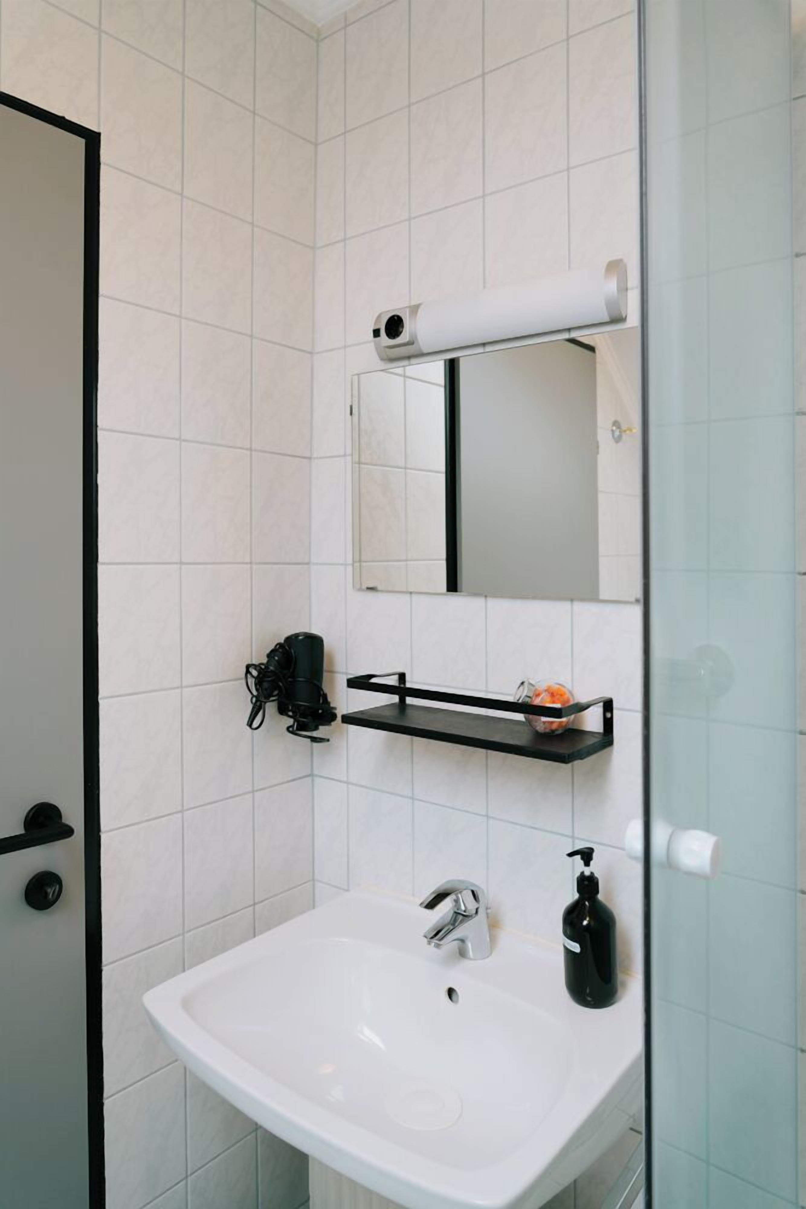 Een moderne badkamer met een wit wastafelmeubel, een spiegel, een zeepdispenser en een douchegedeelte.
