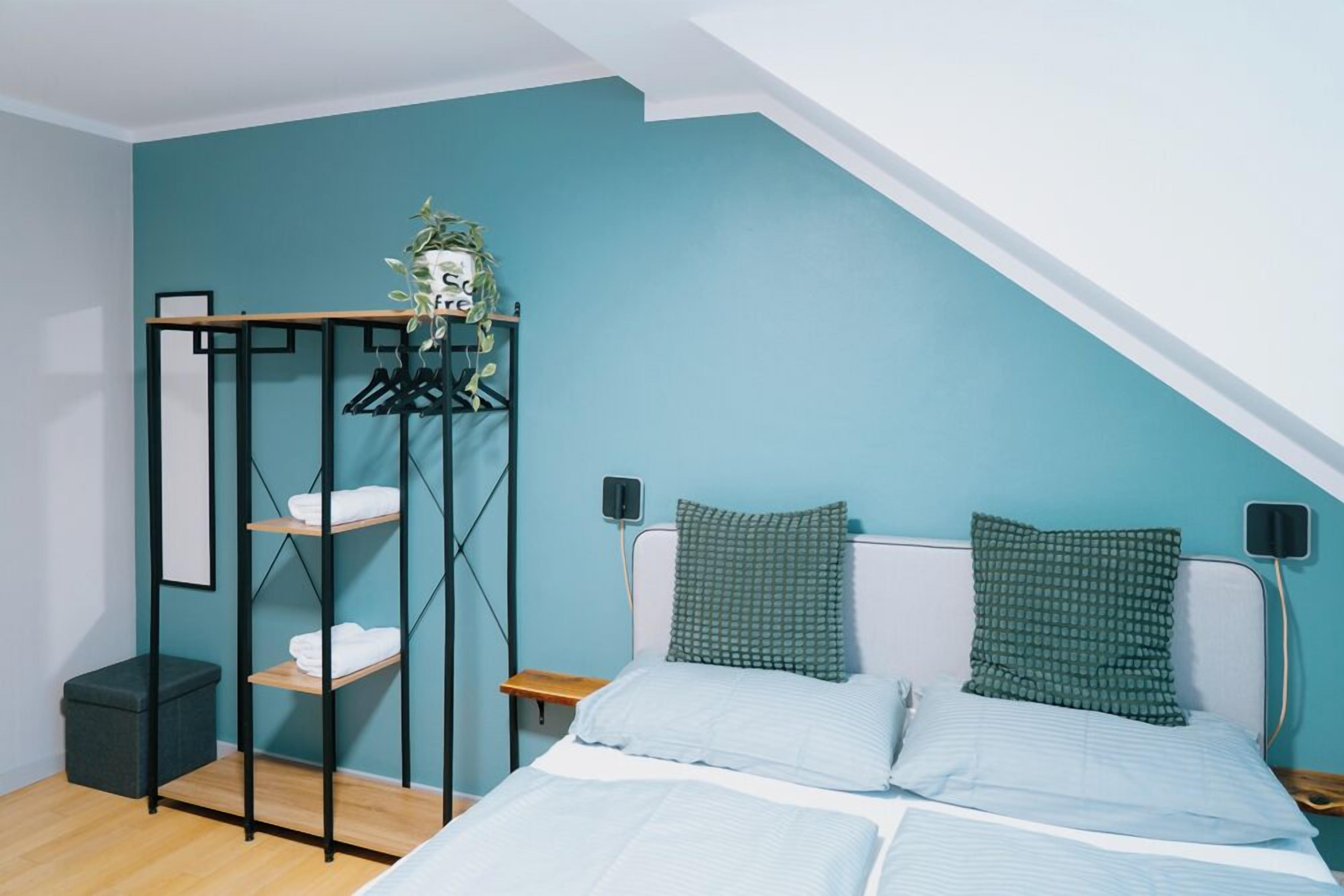 Een slaapkamer met een bed, twee kussens, een wandplank met handdoeken, een klein nachtkastje en een nachtkastje.