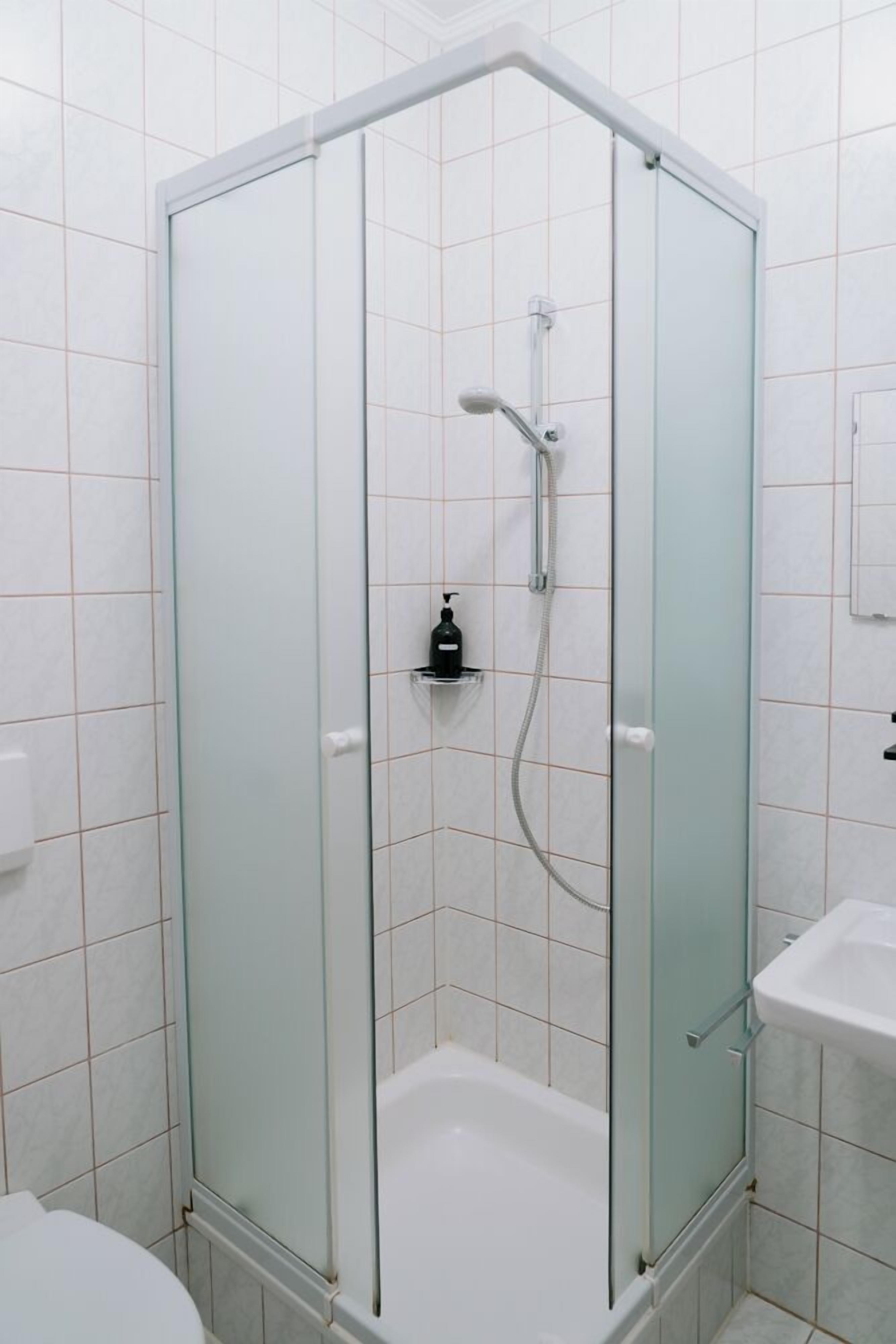 A glass-enclosed shower stall with a handheld showerhead and a handheld faucet.