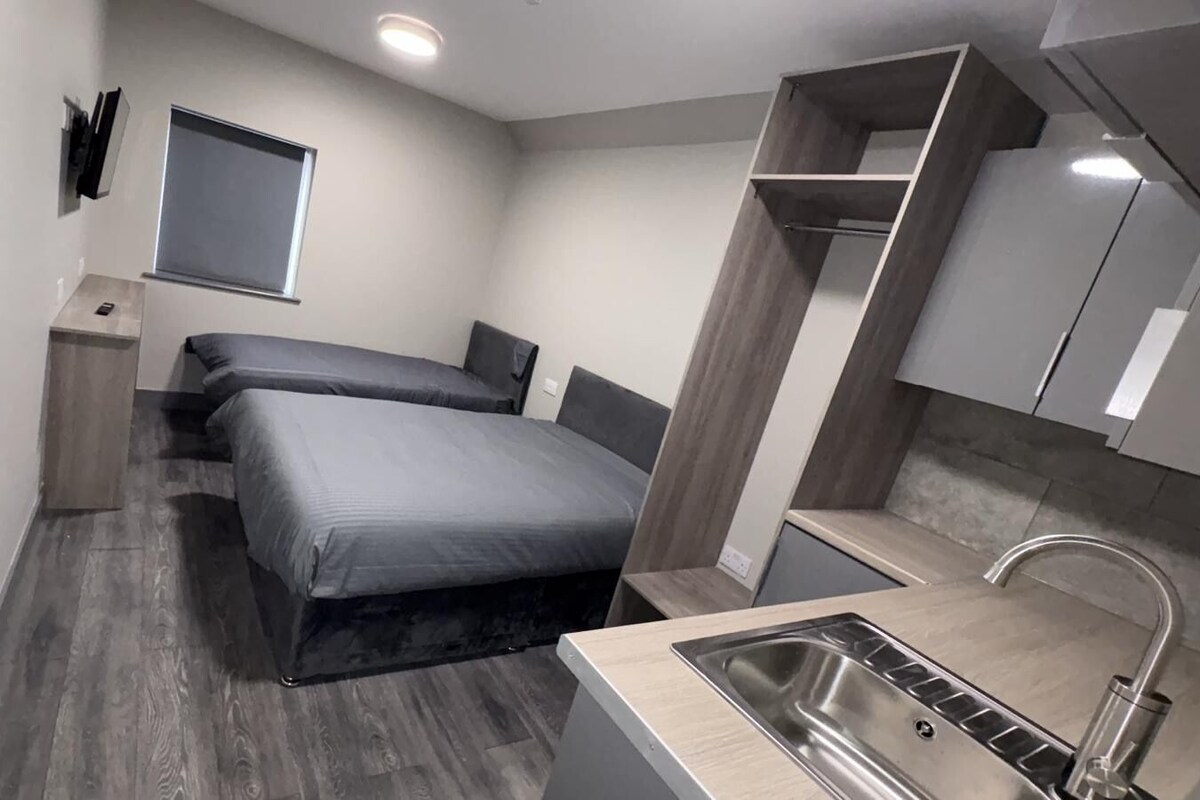 A compact hotel room with a bed, a small kitchenette, and a window.