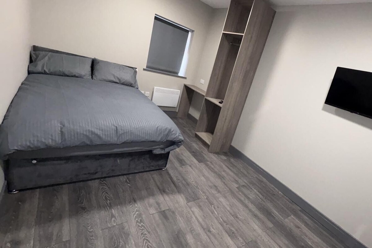 A bedroom with a bed, a TV mounted on the wall, and a window.