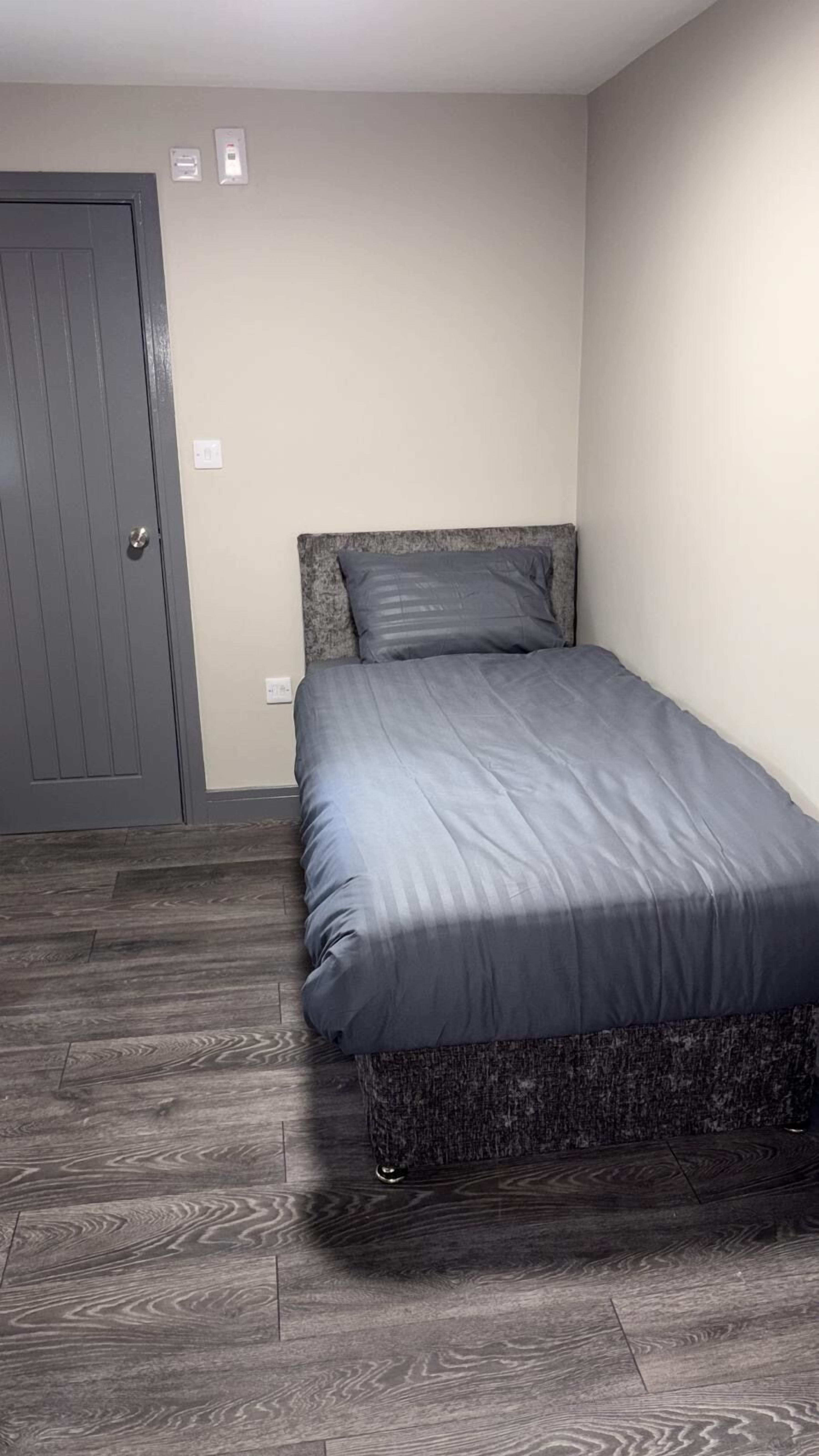 Un dormitorio con cama, puerta e interruptor de pared.