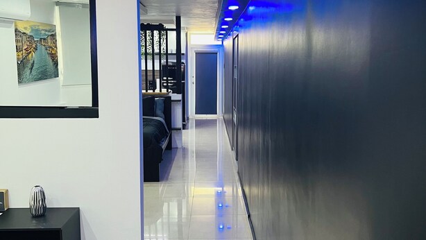 A modern hallway with a black reception desk, a painting of a canal, and a door leading to a seating area.