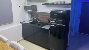 A compact kitchen with a black refrigerator, a microwave, and a sink. There are cabinets below the countertop and a small shelf above the sink.