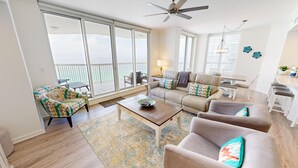 A spacious living room with a large sliding glass door leading to a balcony, a sofa, a coffee table, and a dining area. - Stunning Views SBT 1006W (Destin)