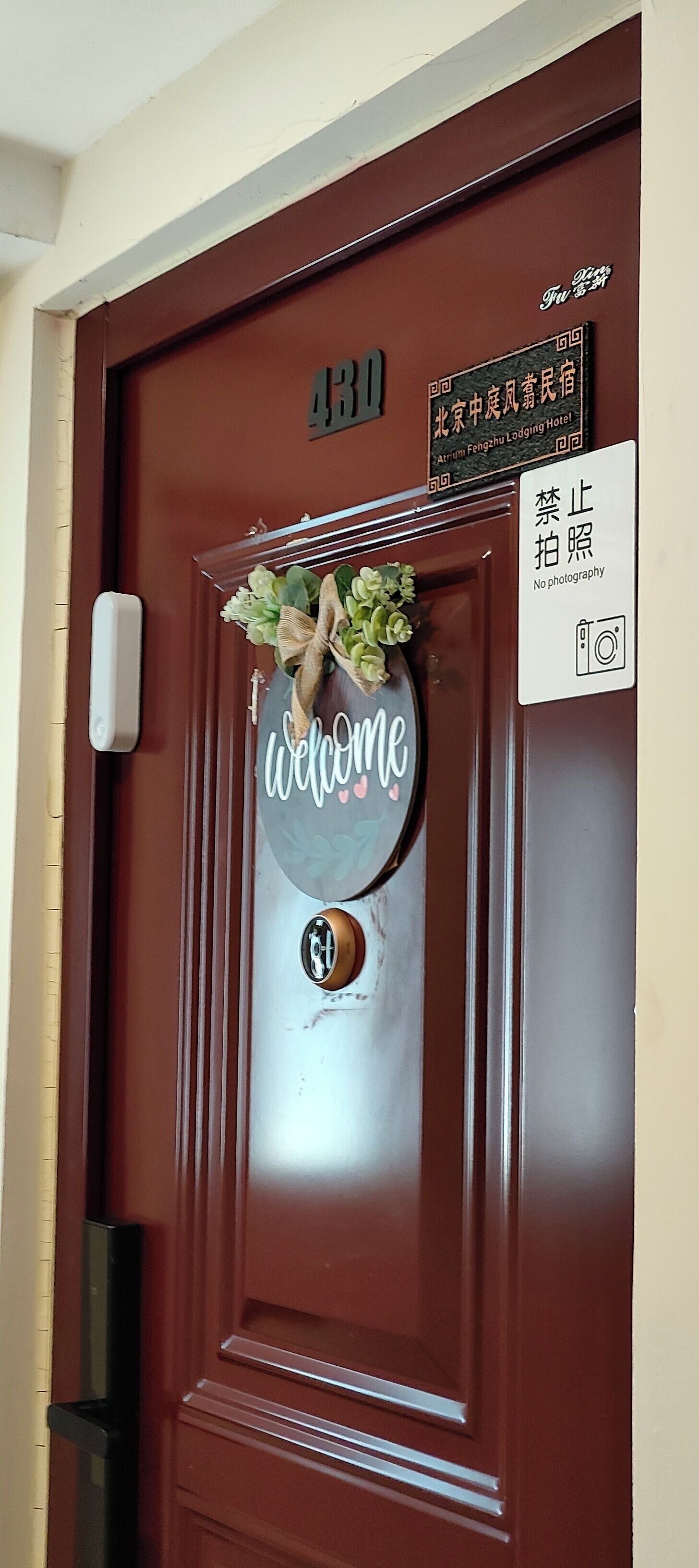 A brown hotel door with a welcome sign, a no photography sign, and a room number sign.