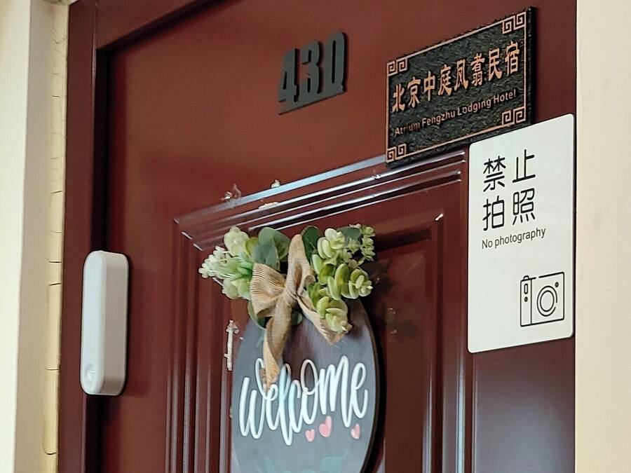 A brown hotel door with a welcome sign, a no photography sign, and a room number sign.