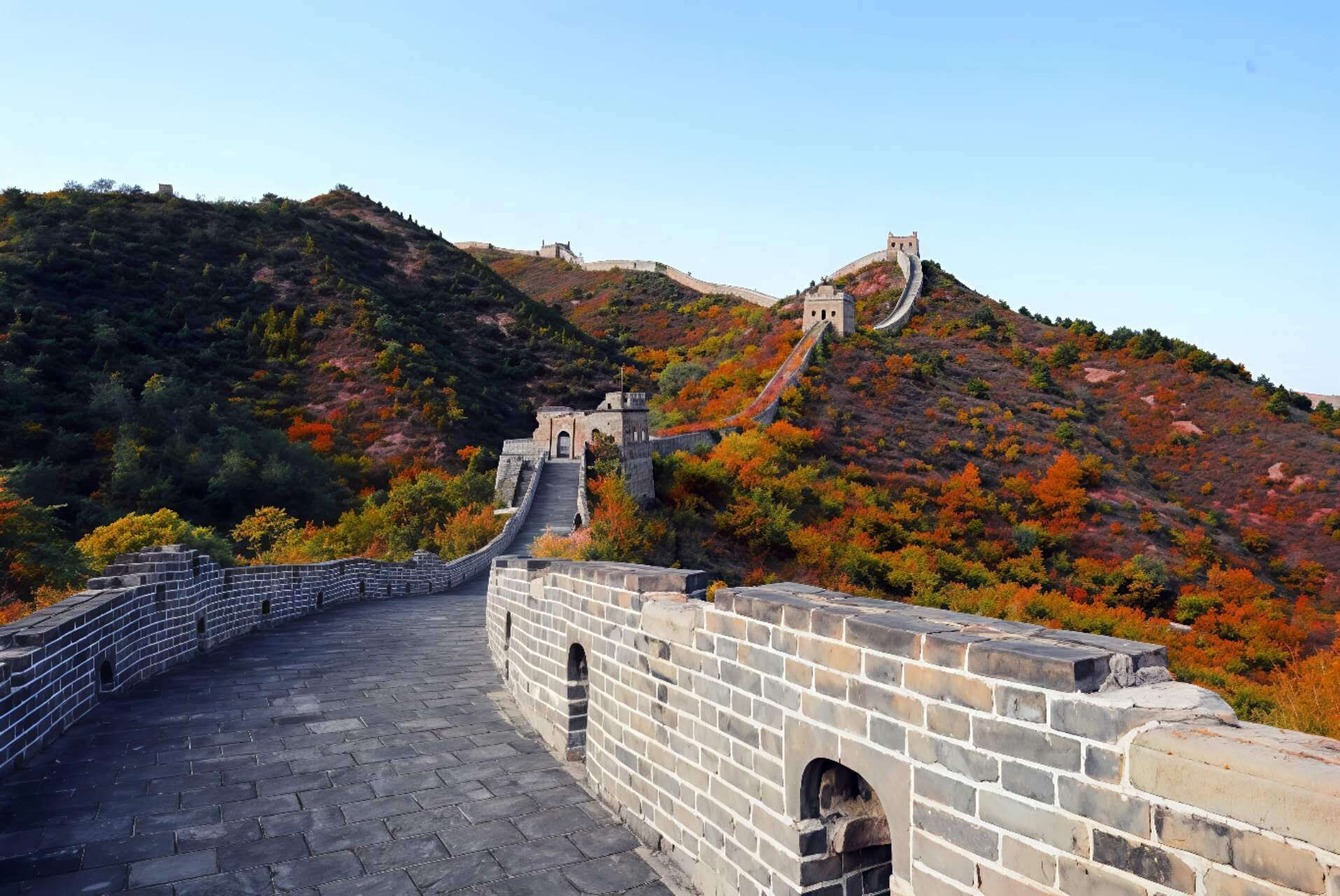 A section of the Great Wall of China with a stone pathway and watchtowers, surrounded by autumn-colored vegetation.